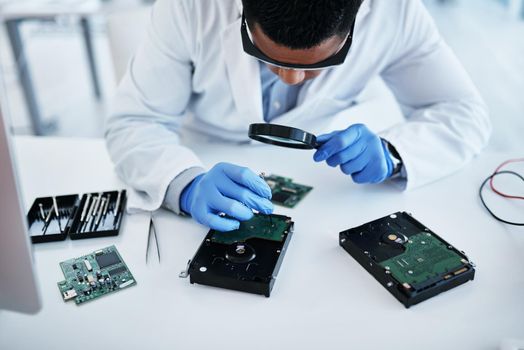 Once hes done, itll be better than before. Shot of a young man using a screwdriver and magnifying glass while repairing computer hardware in a laboratory.