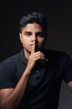Silence is the best answer. Studio shot of a young man posing with his finger on his lips.
