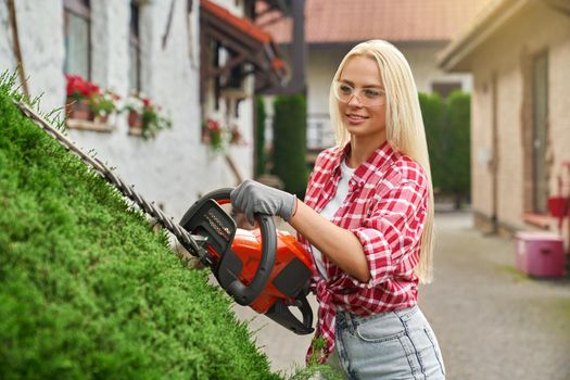 Woman using petrol hedge trimmer for cutting bushes