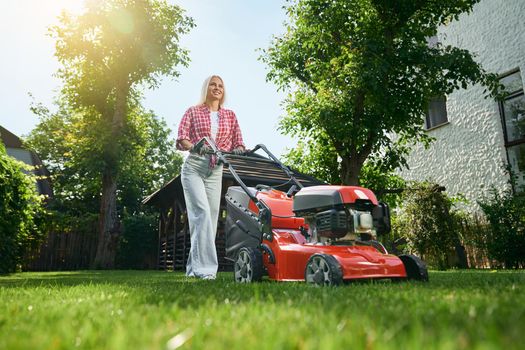 Woman using lawn mower for cutting grass on back yard