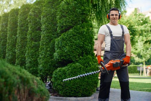 Man holding electric trimmer while standing at garden