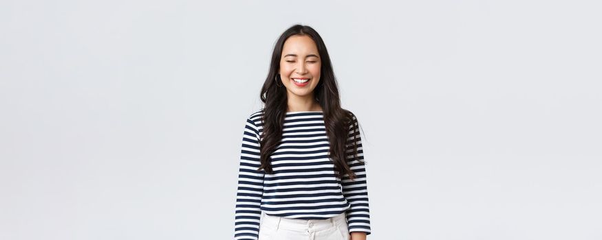 Lifestyle, people emotions and casual concept. Carefree, happy pretty asian woman in striped shirt close eyes and laughing sincere, having fun, funny moment, standing white background