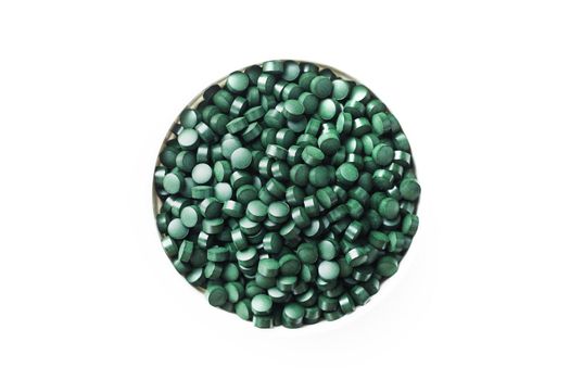 Green tablets made of natural organic spirulina in a cup on a white background with free space