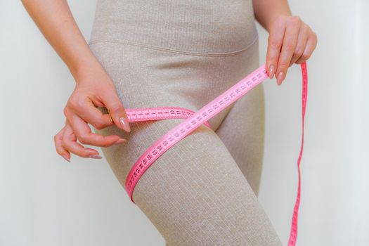 Cropped view of slim woman measuring her leg with tape measure at home, close-up. An unrecognizable European woman checks the result of a weight loss diet or liposuction indoors. Healthy lifestyle.