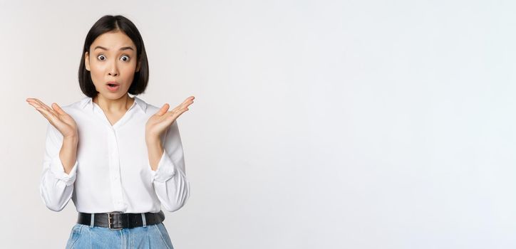 Image of asian female model looking surprised, staring amazed, reacting at surprise big news, standing over white background