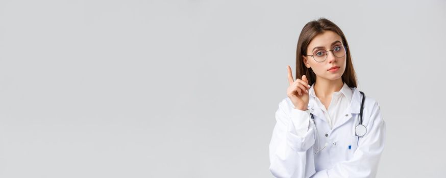 Healthcare workers, medicine, insurance and covid-19 pandemic concept. Smart professional female doctor in white scrubs and glasses, have idea, suggestion, raise index finger eureka sign