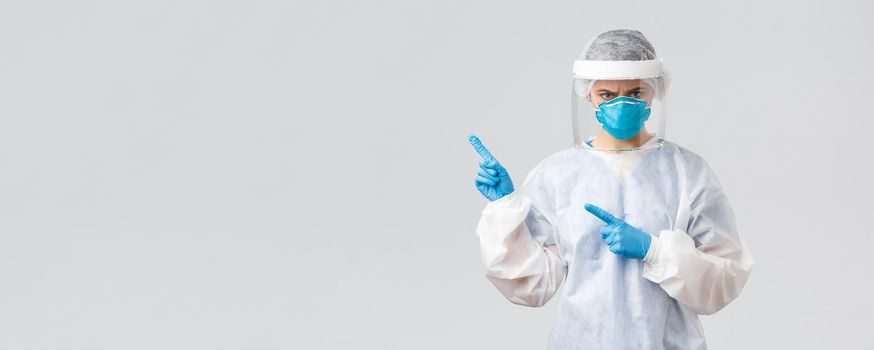 Covid-19, preventing virus, health, healthcare workers and quarantine concept. Angry frowning doctor or nurse in personal equipment, medical suit, respirator and gloves, pointing finger bad news