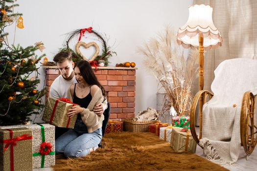 Viewing and arranging gift packages. Couple in love with a gift sits under the Christmas tree. A unique Christmas atmosphere.