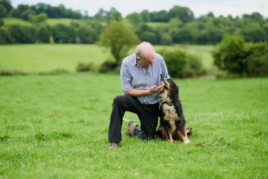 My closest friend. Shot of a cheerful mature farmer kneeling and holding his pet dog outside on a green field.