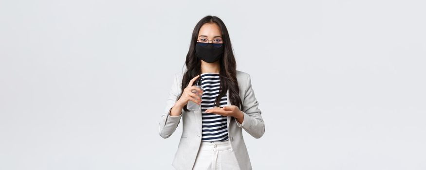 Business, finance and employment, covid-19 preventing virus and social distancing concept. Asian female entrepreneur in face mask apply hand sanitizer to wash hands while at work