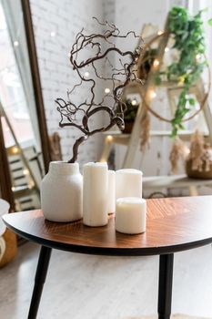 white candles on wooden coffee table in cozy living room interior.Stylish scandinavian living room.Candle and plant in vase on small wooden table in front of scandinavian designed sofa. boho home interior decor.