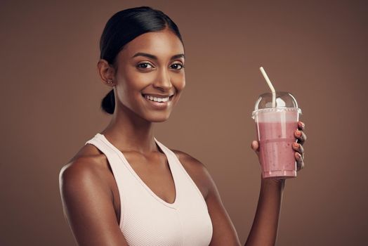 Focused on my health with each smoothie. Shot of an attractive young woman standing alone in the studio and drinking a smoothie.