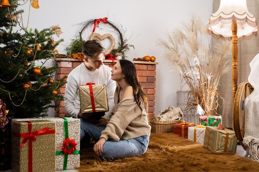 Viewing and arranging gift packages. Couple in love with a gift sits under the Christmas tree. A unique Christmas atmosphere.