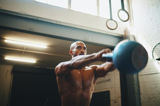 Total body power. Low angle shot of a muscular young man exercising with a kettlebell in a gym.