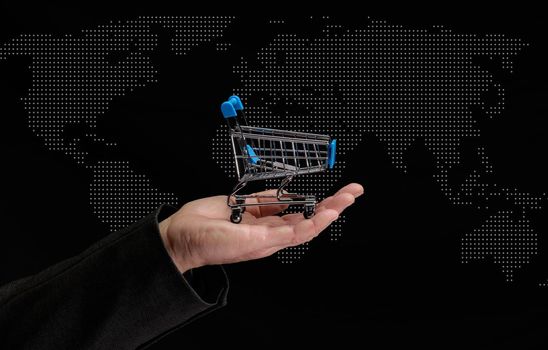 man's hand holds a miniature shopping cart on a dark background, concept of the start of world sales