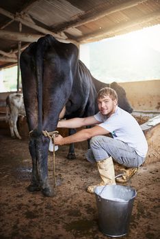 Where did you think milk came from. Full length portrait of a young male farmhand milking a cow in the barn.