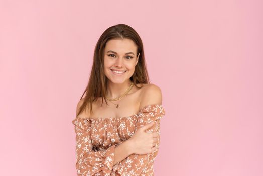 Pretty young woman in a beige dress on a pink background with copy space. Summer concept.