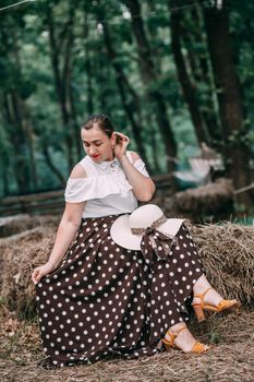 photo of a young smiling blonde, in a white blouse and skirt, on the hay in a summer forest
