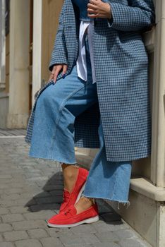Woman in a red stylish suede loafer shoes, blue jeanse, white shirt and trendy checkered coat posing on the street.