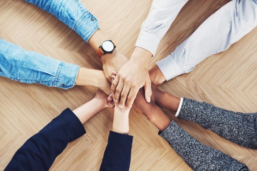 Its easier if we do it together. High angle shot of a group of unidentifiable businesspeople joining their hands together in unity.