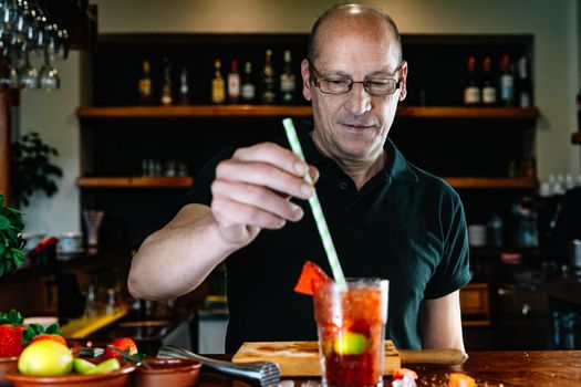Experienced bartender shaking a cocktail in a crystal glass with ice and fruit. Preparing a cocktail for customers