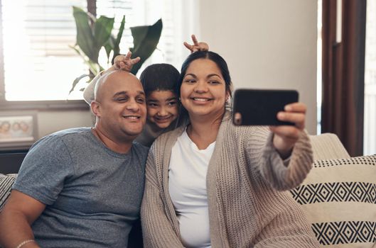 All we have is one another. Shot of a happy young family taking selfies with a smartphone on the sofa at home.