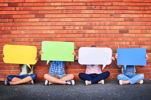 Shot of a group of young children holding speech bubbles against a brick wall.