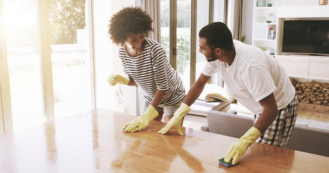 We make a great team. Shot of a cheerful young couple cleaning the surface of a table with cleaning equipment together at home.