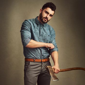 Tough and tempting. Studio shot of a young man posing with an axe against a green background.