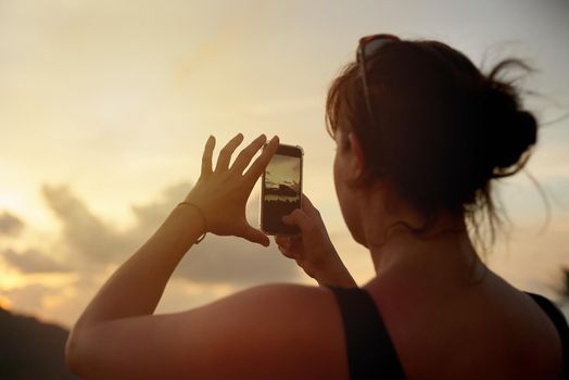 I cant wait to share this view. Shot of a young woman photographing a tropical view with her cellphone while on holiday.