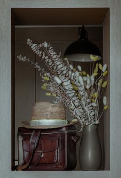 Straw fedora hat on Vintage brown leather bag and Dried flowers in ceramic vase.