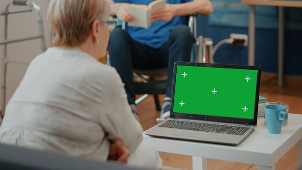 Old woman with disability analyzing green screen on computer