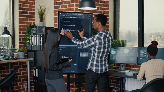 Software engineers analyzing code on wall screen tv comparing errors using digital tablet