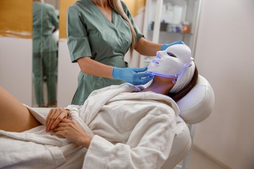 Woman getting cosmetic procedure with LED facial mask. Photon therapy