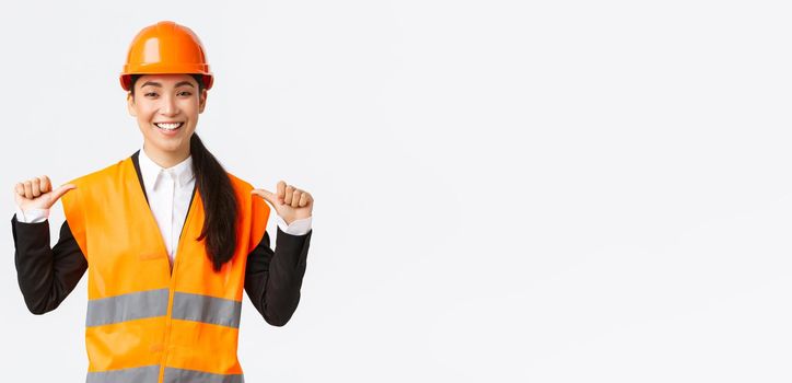 Successful proud smiling asian female construction manager, engineer in safety helmet pointing at herself, show-off. Architect recommend personal assistance, bragging accomplishments