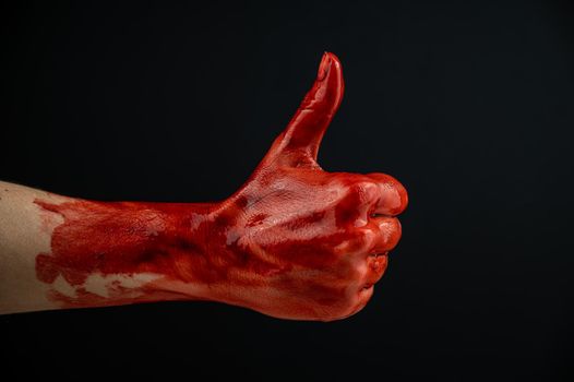 A woman's hand stained with blood shows a thumbs up on a black background.