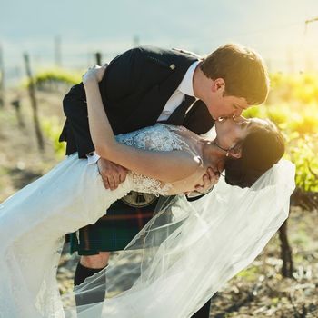 What a stunning kiss. Shot of a cheerful bride and groom sharing a kiss together outside next to vineyards during the day.