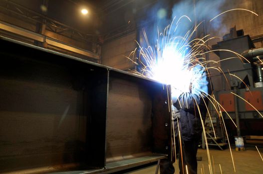 A worker electric welder cooks steel in a semi-automatic factory.