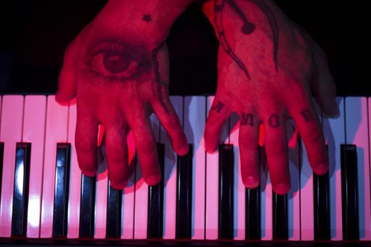Tattooed mans hands on the keyboard of a piano