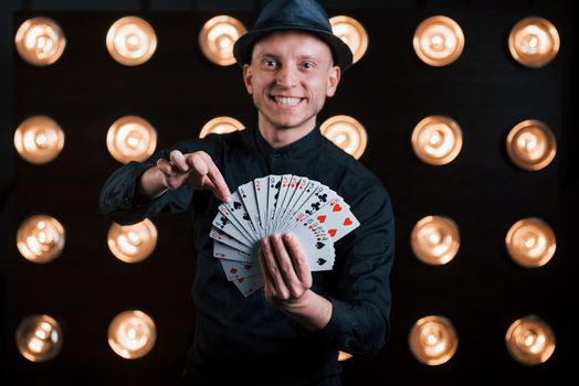 He's takes your card. Magician in black suit standing in the room with special lighting at backstage
