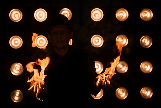 Dangerous beauty of the fire in the hands. Professional magician showing trick. Light bulbs on background