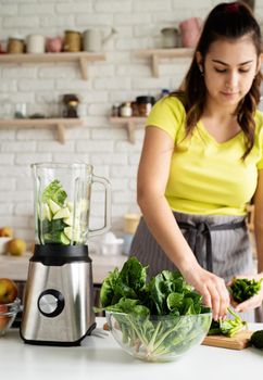 Young woman making green spinach smoothie at home kitchen