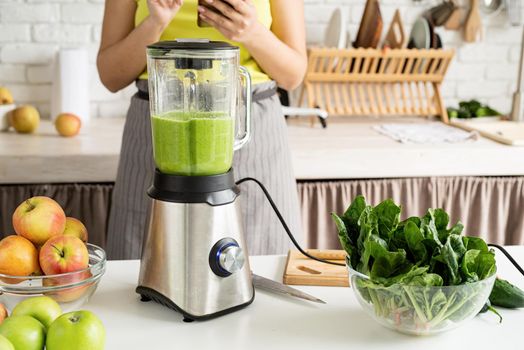 Young woman making green smoothie at home kitchen