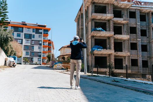 Man taking cellphone photo of development site. Architect engineer estimates building progress. Insurance agent inspects building. Journalist blogger pictures unfinished cancelled house construction