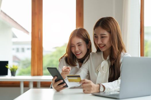 Two asian girlfriends shopping online with smart phone and credit card at home.