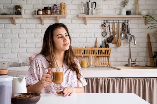 young woman in lovely pajamas drinking coffee at home kitchen