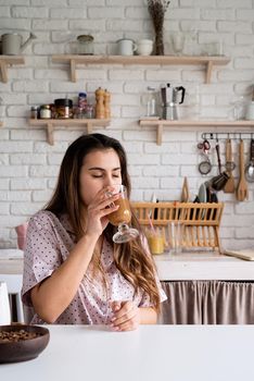 young woman in lovely pajamas drinking coffee at home kitchen