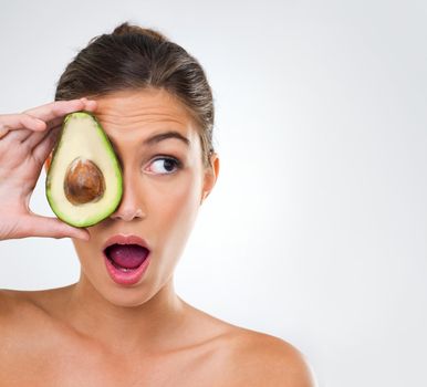 Improving my skin, one avocado at a time. Shot of a gorgeous young woman holding half an avocado over the side of her face.