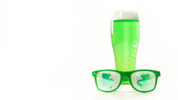 A glass of green beer and funny glasses for st patrick's day on a white background. Traditional Irish drink for a holiday. Copy spase.