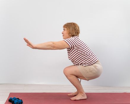 Elderly woman doing squats on a white background. The old lady is doing exercises for her health